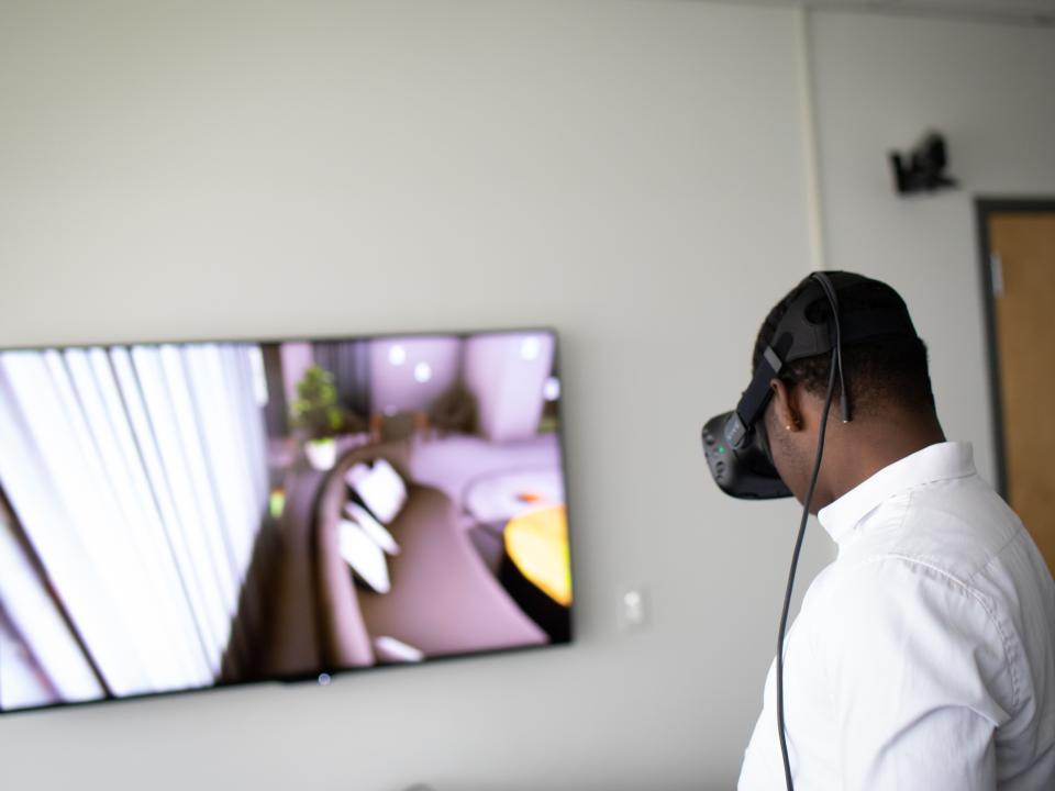 A student wearing a VR headset in a simulation that is also displayed on a monitor