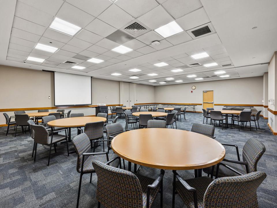 Talon room 218 with round tables and built in projector screen.