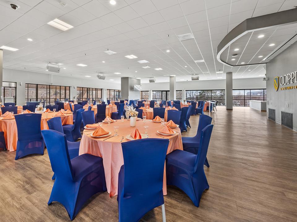 View of the Tawes Ballroom from the front right. Stage area is to the right and tables are to the left with as wall of tall windows overlooking the campus in the background.