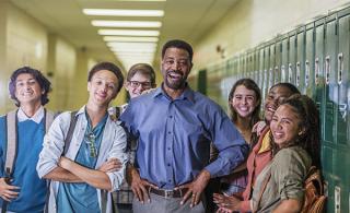 A male school administration stands with a group of students in a school hallway