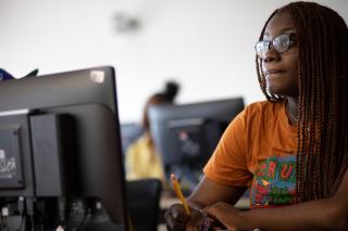 A Coppin student sitting in front of a classroom computer takes notes while listening to a lecture