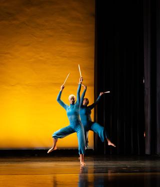 Coppin dancer performance two dancers in blue jumpsuits align on stage with one leg and arms raised